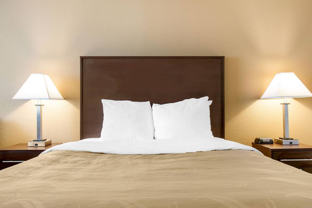 A neatly made bed with white linens, two bedside lamps, and a wooden headboard.