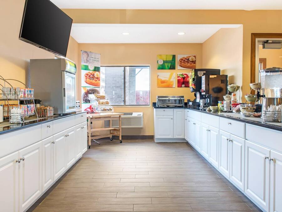 Une cuisine avec des meubles blancs, une machine à café, un réfrigérateur et une fenêtre.