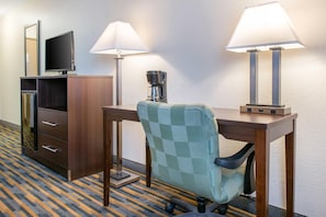 A hotel room with a desk, two lamps, a coffee maker, a television, and a wardrobe. - Quality Inn Noblesville - Indianapolis (Noblesville)