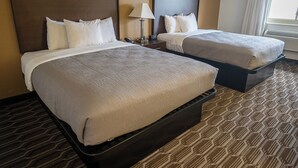 A hotel room with two beds, a nightstand with a lamp, and a window with curtains. - Quality Inn Noblesville - Indianapolis (Noblesville)