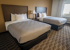 A hotel room with two beds, a nightstand with a lamp, and a window with curtains. - Quality Inn Noblesville - Indianapolis (Noblesville)