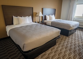 Habitación de hotel con dos camas, una mesita de noche con lámpara y una ventana con cortinas.