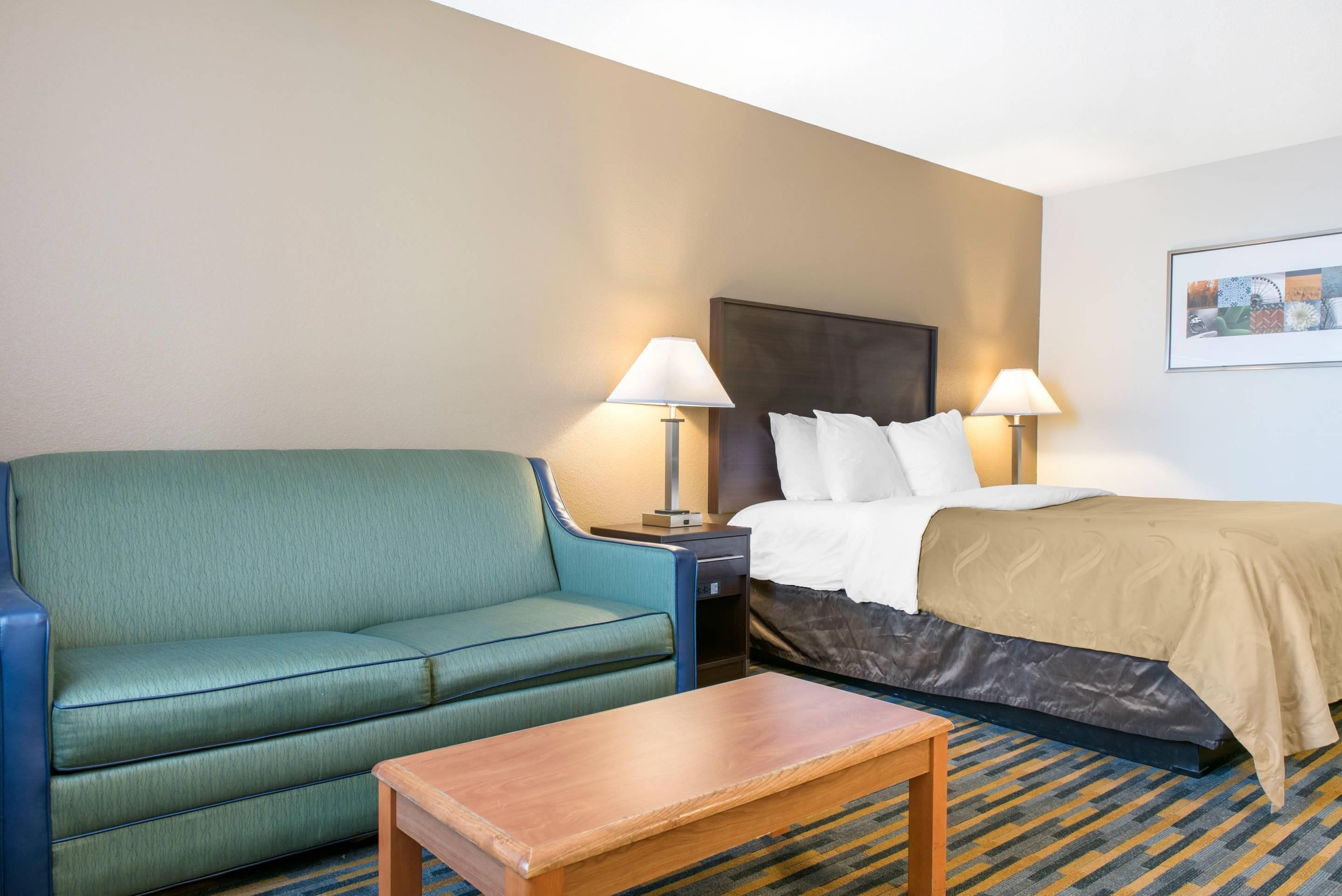 Une chambre d’hôtel avec un lit, un canapé vert, une table en bois et deux lampes de chevet.