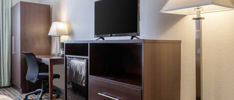 Una camera d'albergo con un letto, una scrivania con una sedia, una televisione, un minibar e una lampada.