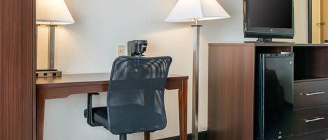 A hotel room with a desk, chair, television, and a minibar.