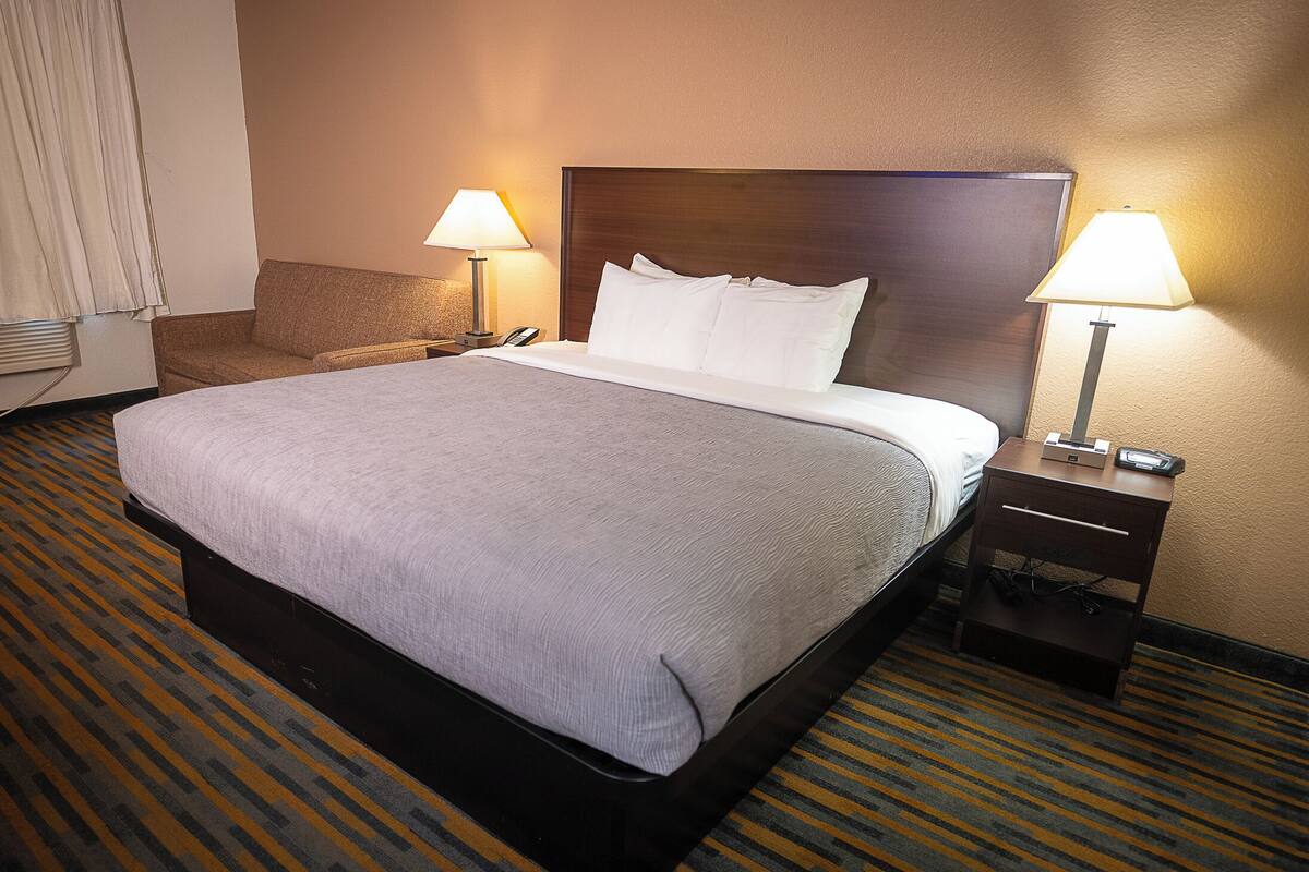 A hotel room with a large bed, two bedside lamps, a nightstand, and a patterned carpet.