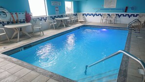 An indoor swimming pool with clear blue water, surrounded by white chairs and a table. - Quality Inn Noblesville - Indianapolis (Noblesville)