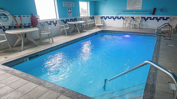 An indoor swimming pool with clear blue water, surrounded by white chairs and a table. - Quality Inn Noblesville - Indianapolis (Noblesville)