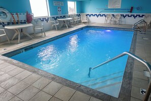 An indoor swimming pool with clear blue water, surrounded by white chairs and a table. - Quality Inn Noblesville - Indianapolis (Noblesville)