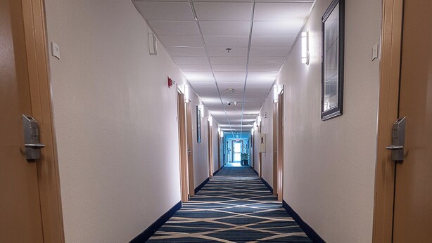 A hotel hallway with a patterned carpet, doors on both sides, and a light at the end. - Quality Inn Noblesville - Indianapolis (Noblesville)