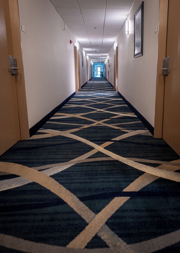 A hotel hallway with a patterned carpet, doors on both sides, and a light at the end. - Quality Inn Noblesville - Indianapolis (Noblesville)