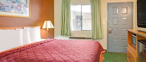 Une chambre d’hôtel avec un lit, une télévision, un bureau et une fenêtre avec des rideaux.