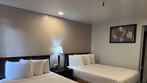 Habitación de hotel con dos camas, una mesita de noche con lámpara, un reloj y un cuadro en la pared.