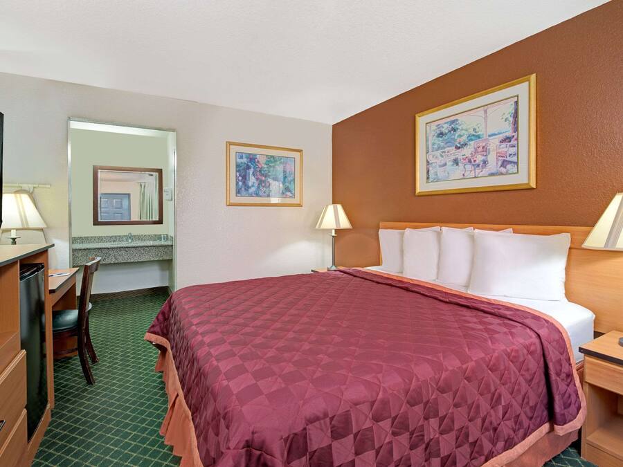 A hotel room with a bed, a desk, a chair, a television, and two paintings on the wall.
