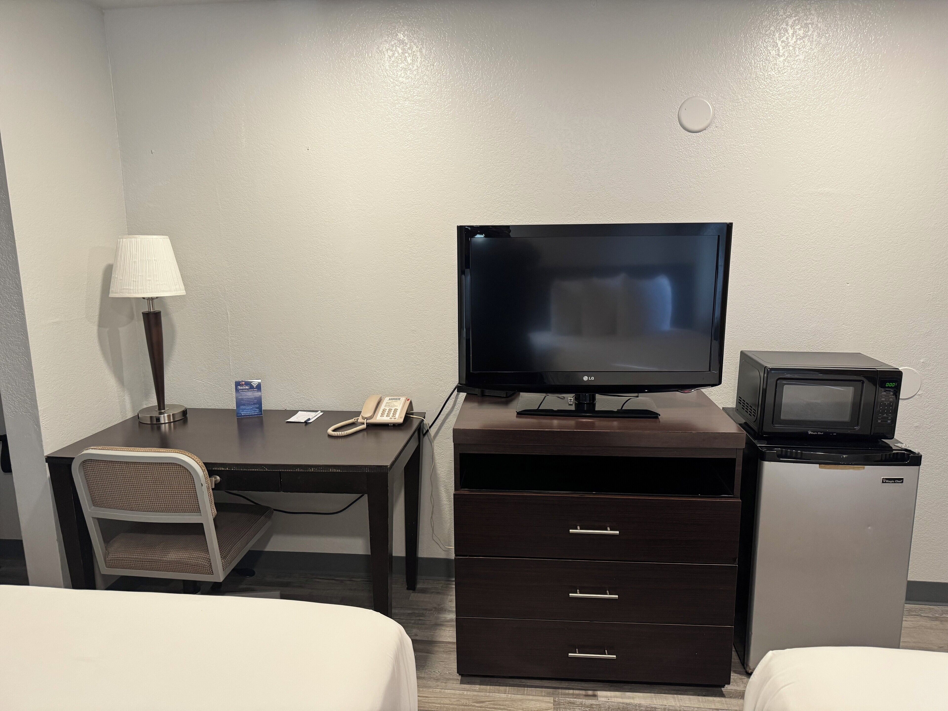 A hotel room with a desk, a television, a microwave, a lamp, and two beds.
