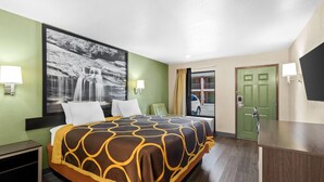 Habitación de hotel con cama, dos lámparas de noche, una puerta verde, una ventana con vista a un coche y una fotografía grande en blanco y negro en la pared.