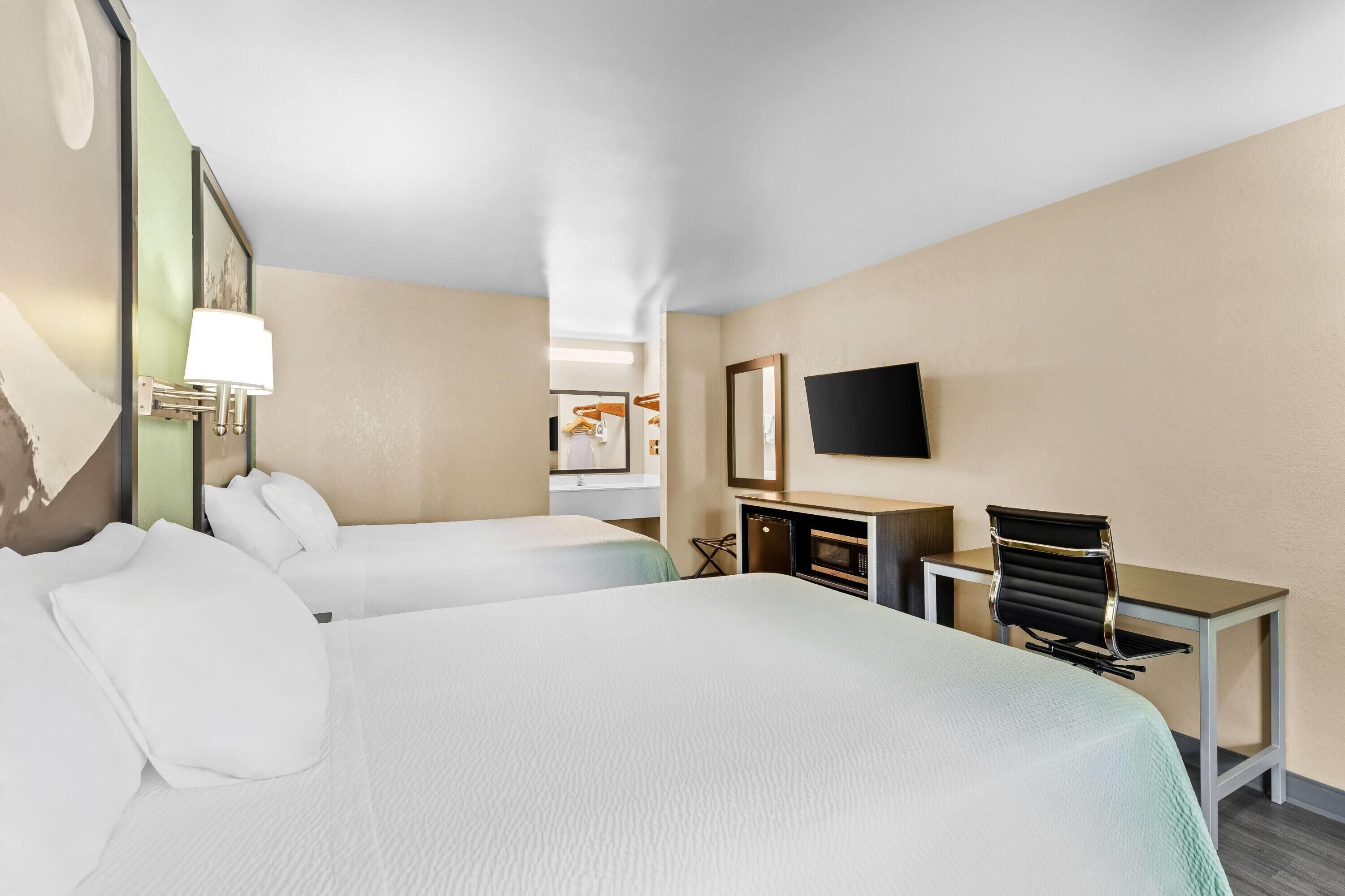 Een hotelkamer met twee bedden, een bureau, een stoel, een televisie en een spiegel.