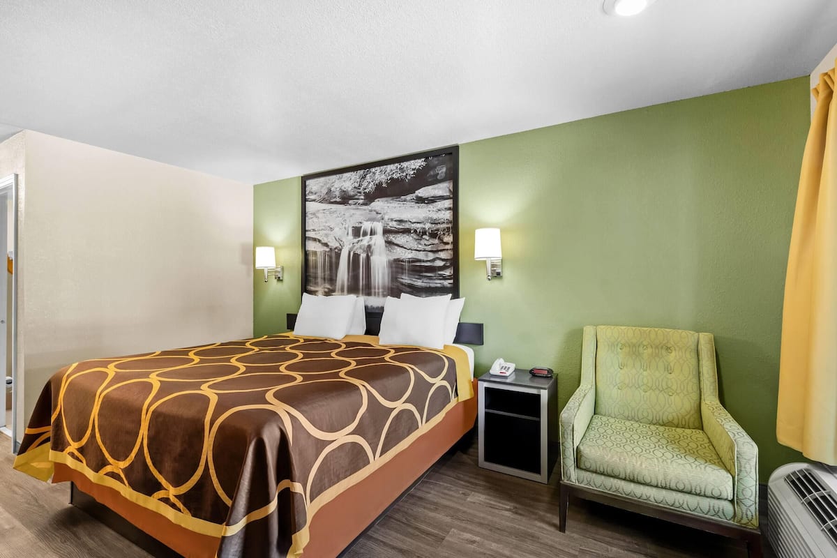 Una habitación de hotel con cama, una silla, una mesita de noche y una lámpara fijada a la pared.