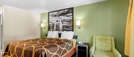 A hotel room with a bed, a chair, a nightstand, and a wall-mounted lamp.