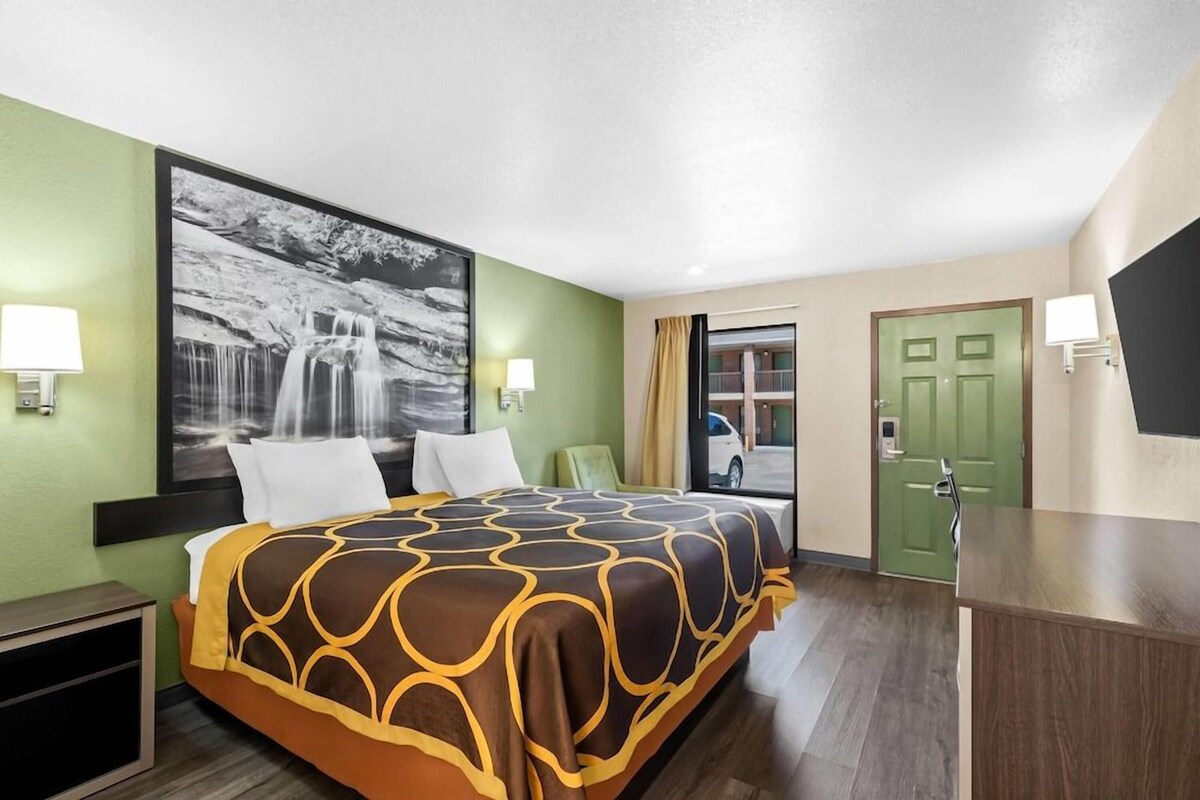A hotel room with a bed, a desk, a chair, a large window, and a door.