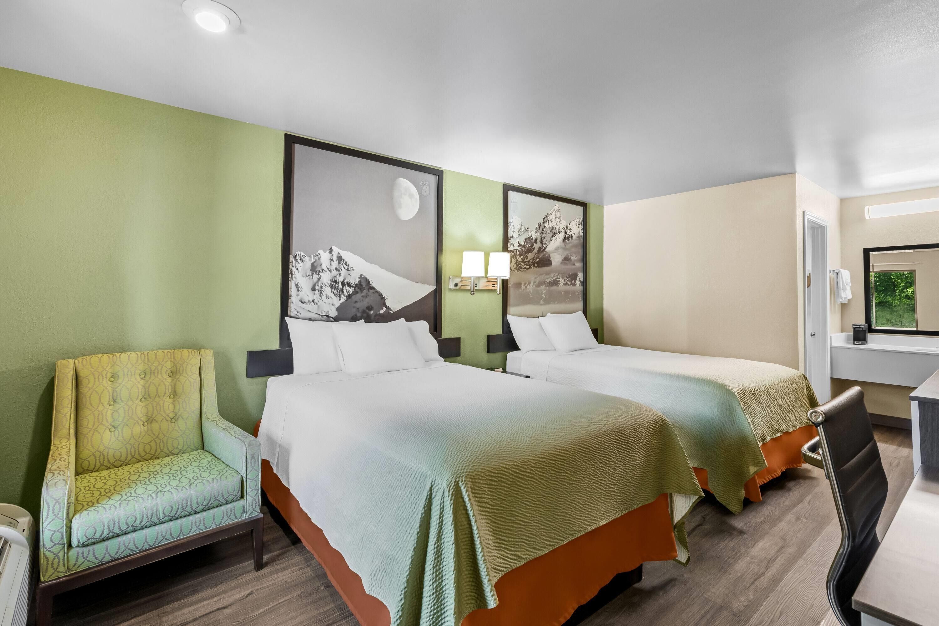 A hotel room with two beds, a chair, a desk, and a window.