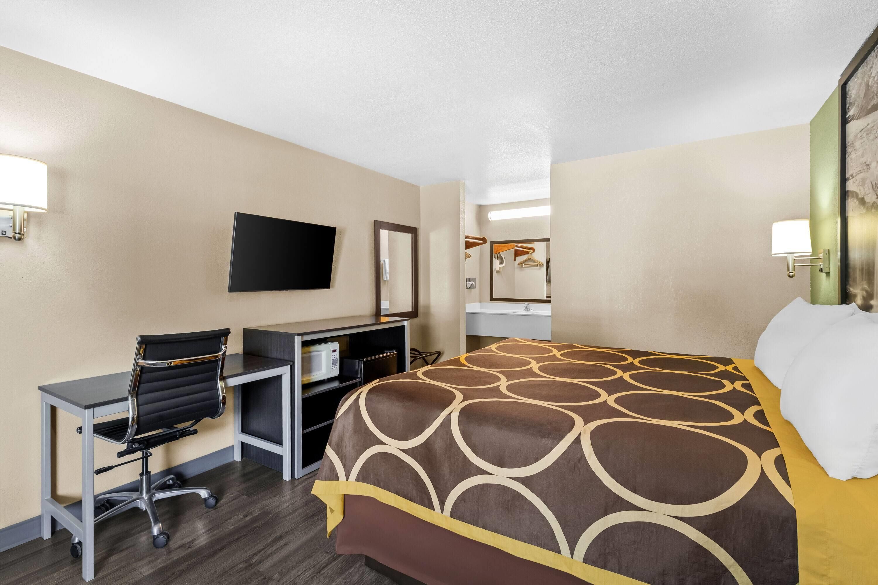 A hotel room with a bed, desk, chair, TV, and a mirror.