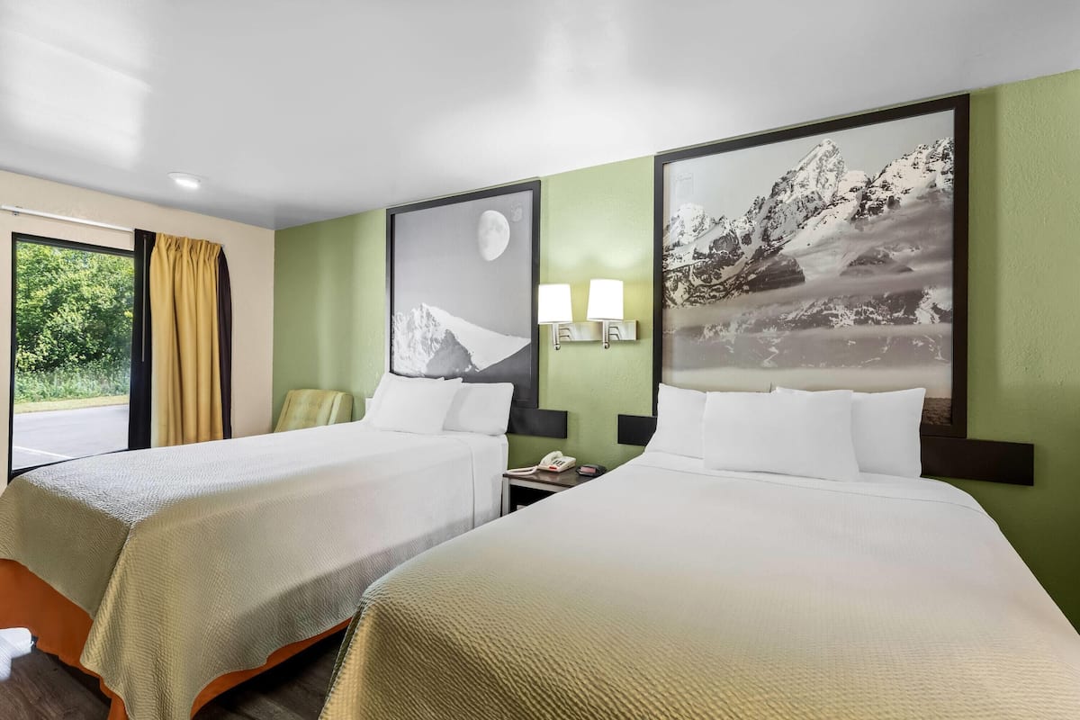 Habitación de hotel con dos camas, una ventana con cortinas y dos lámparas fijadas a la pared.