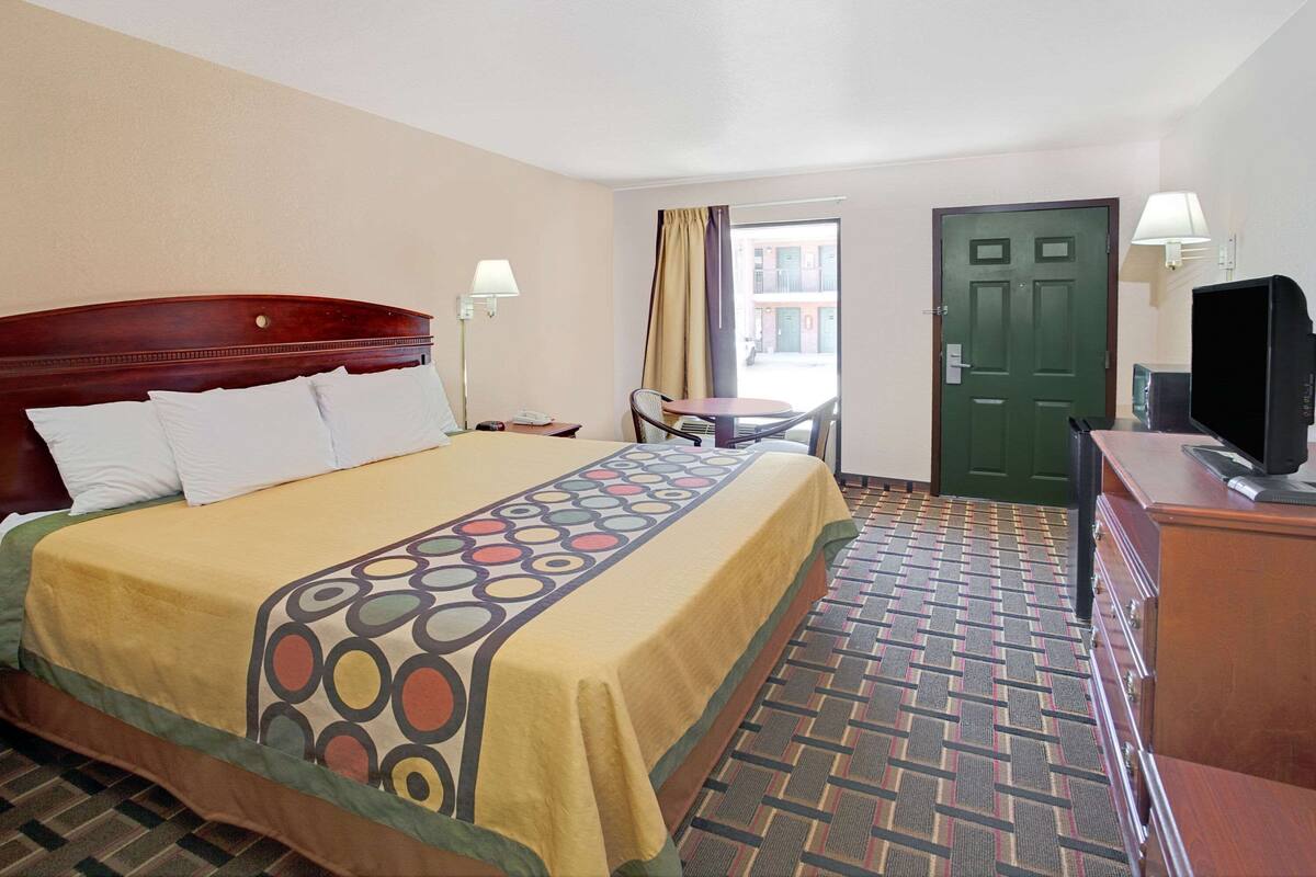 Una habitación de hotel con una cama, un escritorio, una silla, televisión y una puerta.