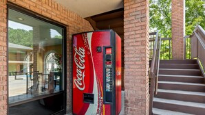 Una máquina expendedora de Coca-Cola frente a un edificio de paredes de ladrillo y una escalera.
