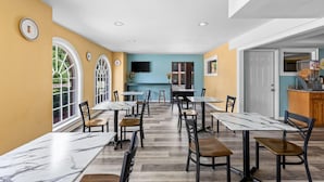 Un comedor con mesas y sillas de mármol, una cocina al fondo y una pared azul.