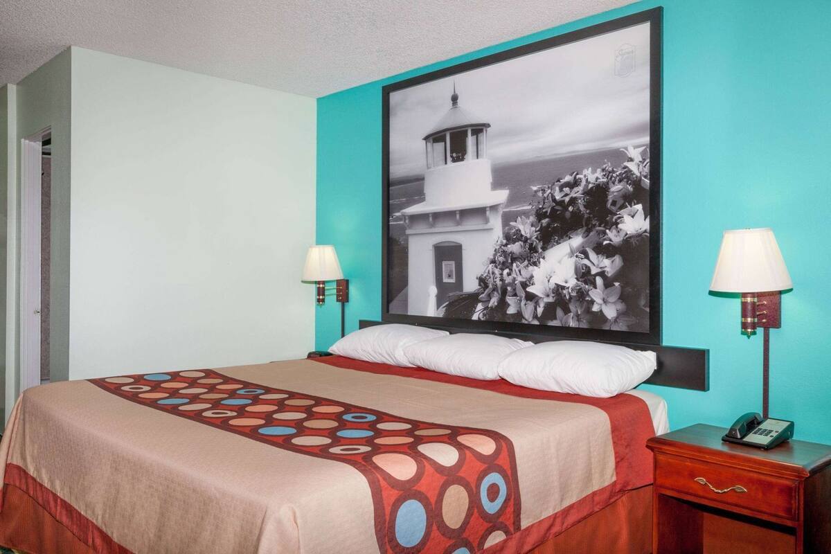 Habitació d'hotel amb llit, dues làmpades de nit, una tauleta de nit amb un telèfon i un quadre gran amb marc a la paret.