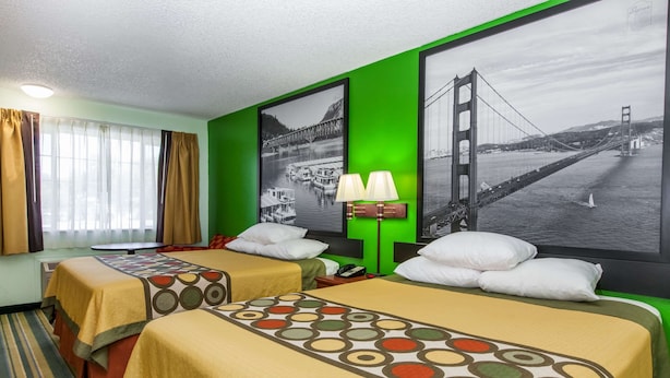 Habitación de hotel con dos camas, un ventanal con cortinas, una lámpara y dos cuadros con imágenes de un puente.
