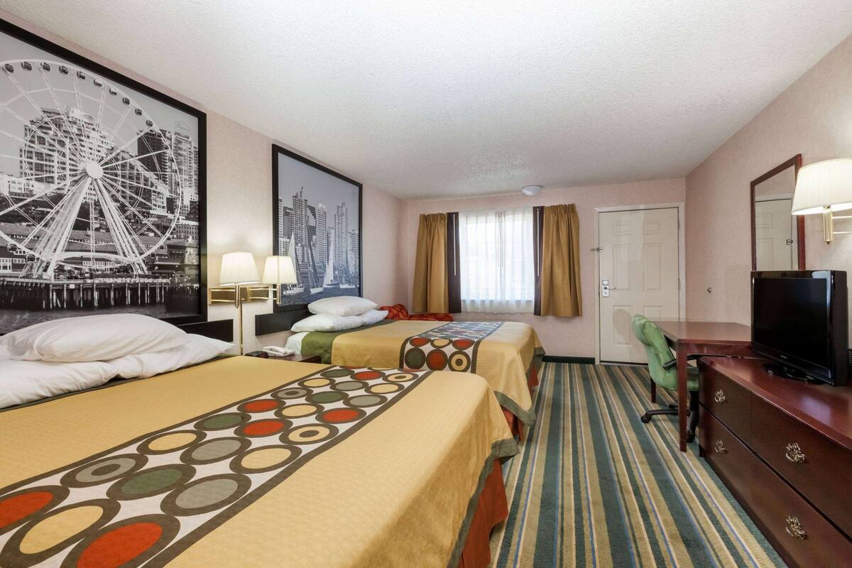 Habitació d'hotel amb dos llits, escriptori, televisió i una finestra gran amb cortines.