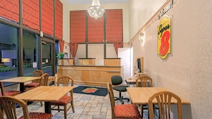Interior de restaurante con mesas y sillas de madera, un mostrador de recepción y un letrero que dice "¡Bienvenido!".