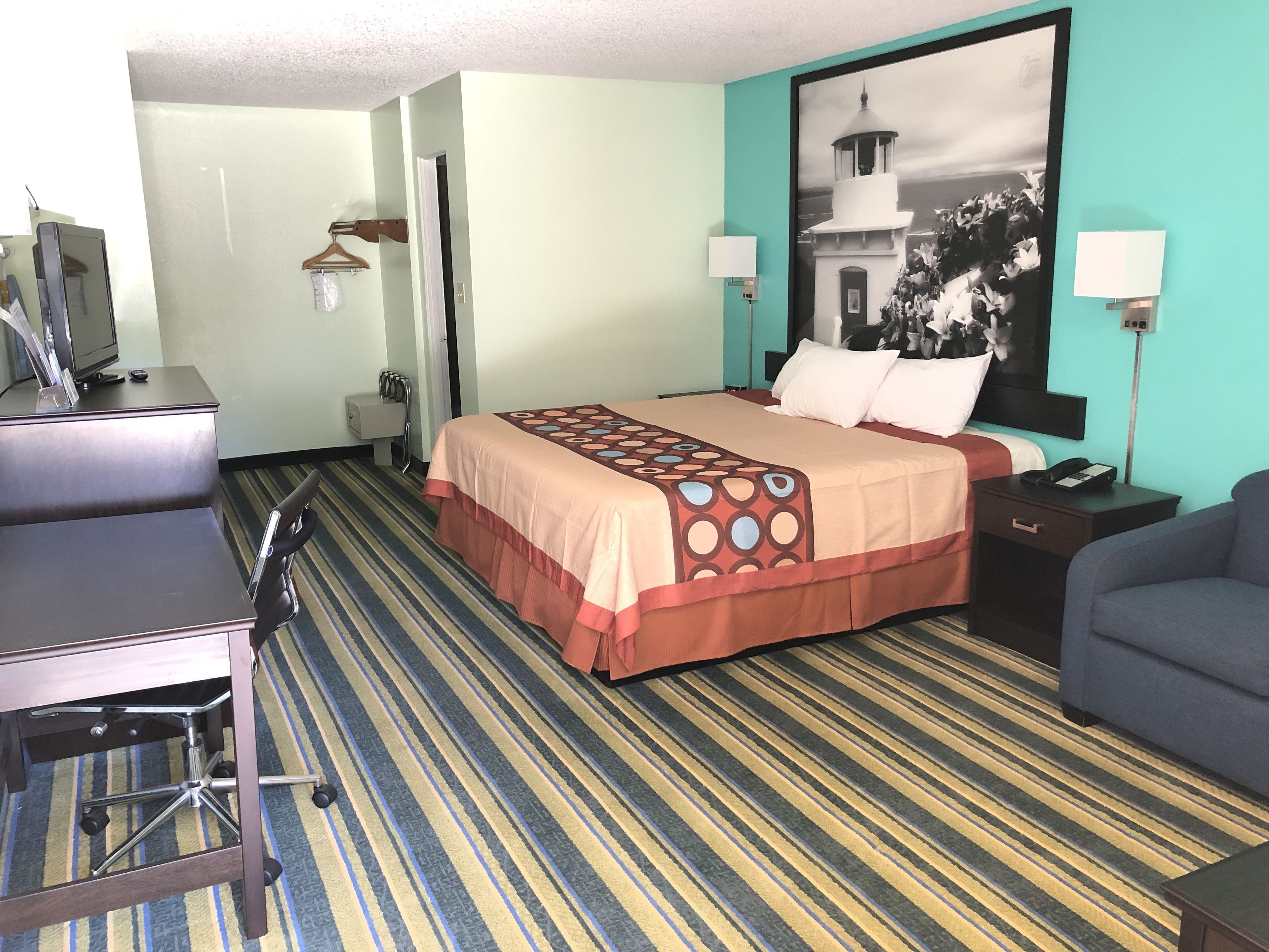 A hotel room with a bed, desk, chair, and a large framed picture on the wall.