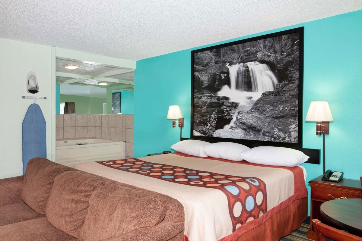 Habitación de hotel con cama, un televisor grande de pared y baño con bañera y espejo.