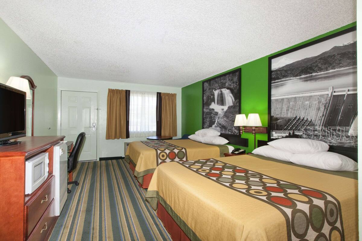 Habitació d'hotel amb dos llits, una escriptori amb televisió, una cadira, una làmpada d'escriptori i una finestra gran amb cortines.