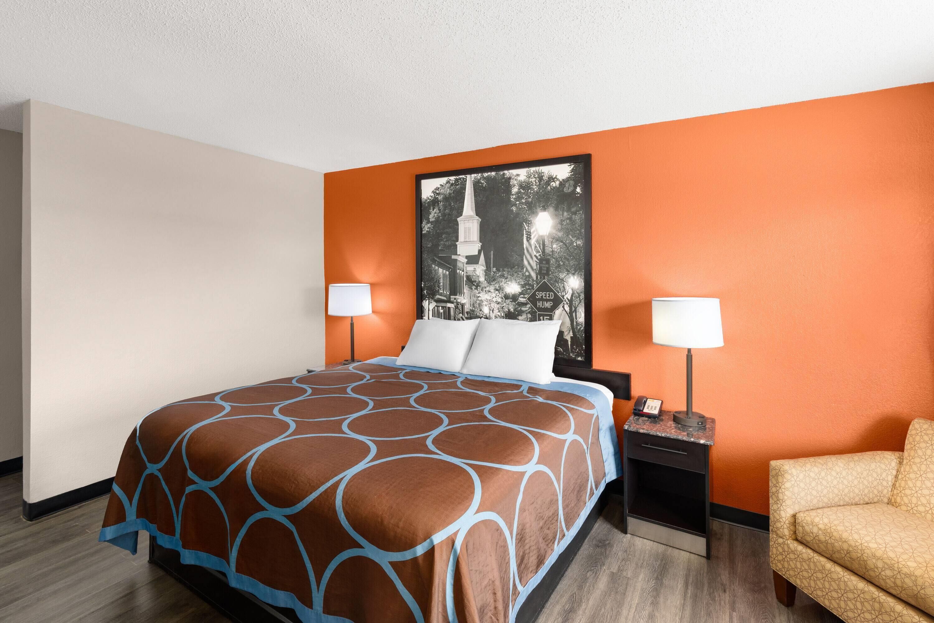 Ein Hotelzimmer mit einem Bett, zwei Nachttischlampen, einem Nachttisch und einem gerahmten Bild an der Wand.