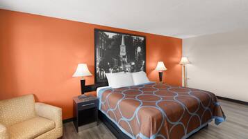 Een hotelkamer met een oranje wand, een bed met een beddeken met een patroon, twee bedlampen, een nachtkastje en een stoel.