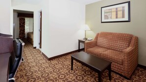 A hotel room with a patterned carpet, a sofa, a coffee table, a lamp, and a framed picture on the wall. - Super 8 by Wyndham Decatur/Dntn/Atlanta Area (Decatur)