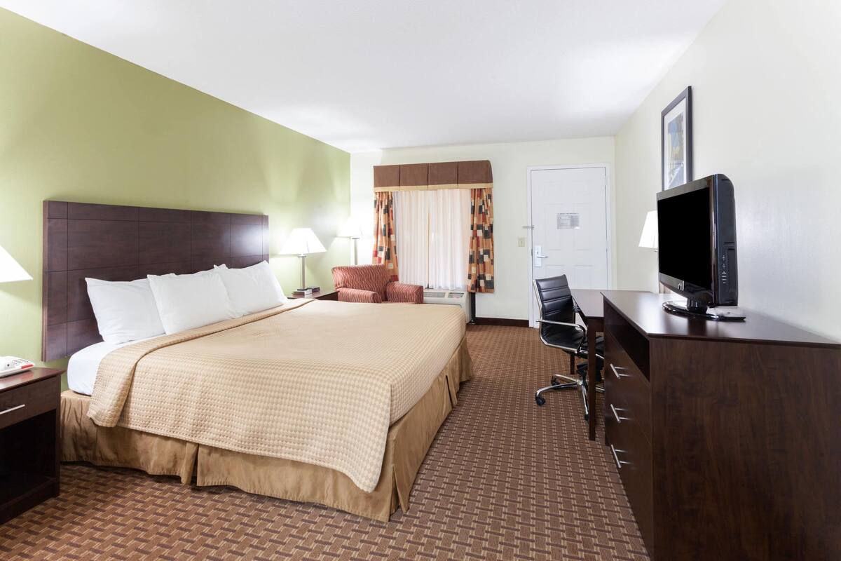 A hotel room with a large bed, a desk with a computer, a chair, and a television.