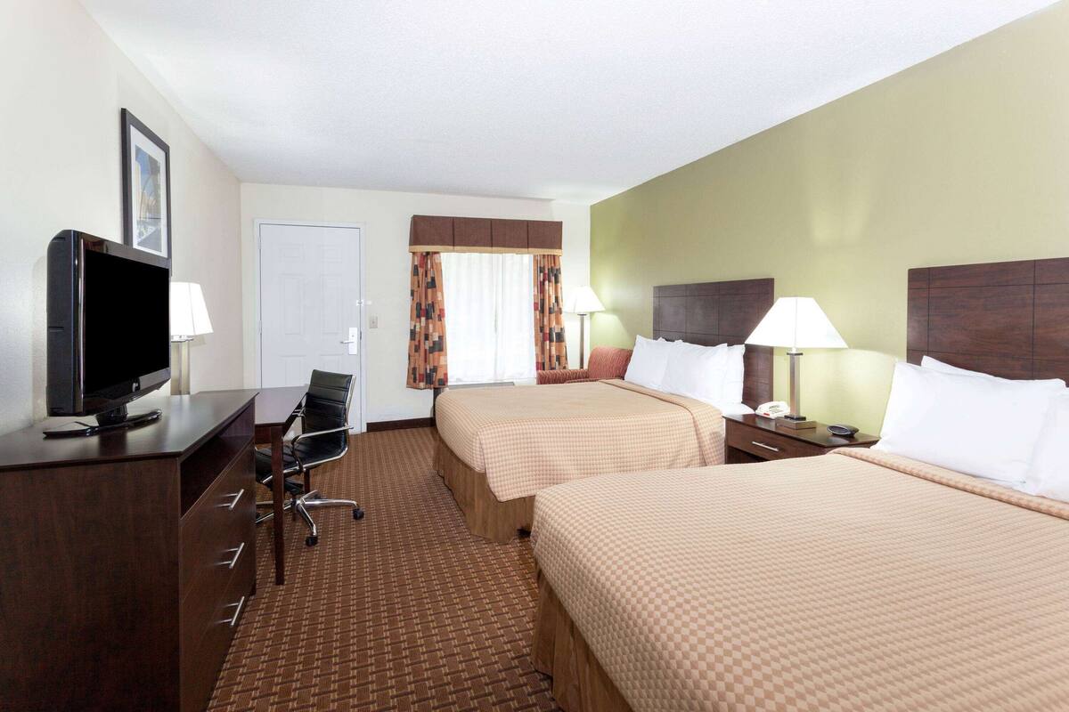 A hotel room with two beds, a desk with a TV, a chair, and a lamp.