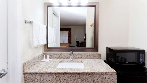A bathroom with a granite countertop, a white sink, a mirror, and a black microwave. - Super 8 by Wyndham Decatur/Dntn/Atlanta Area (Decatur)
