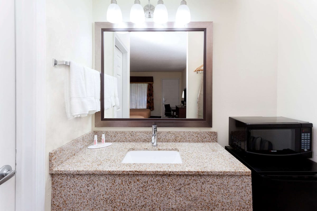 A bathroom with a granite countertop, a white sink, a mirror, and a black microwave.
