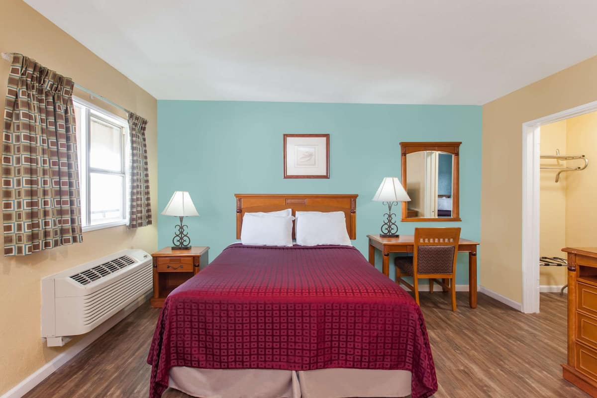A hotel room with a bed, two bedside tables with lamps, a chair, a desk, a mirror, and a radiator.