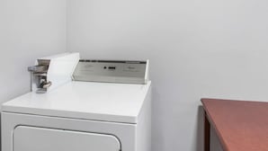 Una lavadora compacta y blanca en una esquina de una habitación con una mesa de madera.