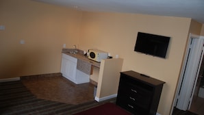 Un espacio habitable compacto con kitchenette, un televisor de pantalla plana montado en la pared y un mueble pequeño.