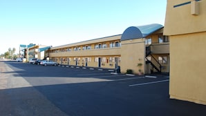 Un motel con una fila de habitaciones, un estacionamiento y un corredor cubierto.