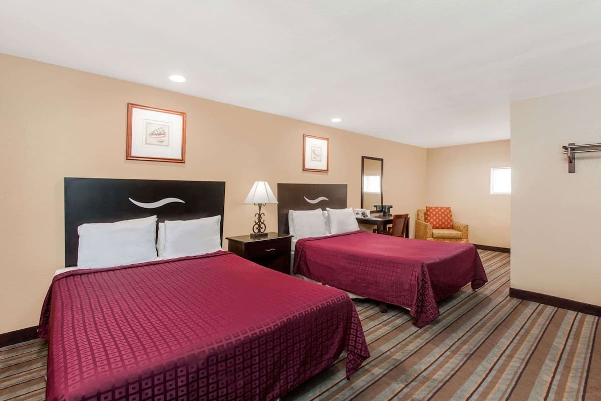 A hotel room with two beds, a desk, a chair, and a mirror.