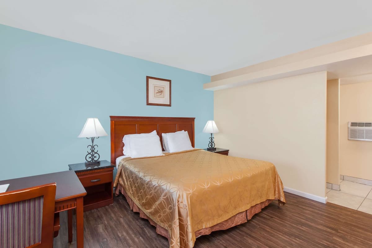 A hotel room with a large bed, two bedside tables with lamps, a wooden nightstand, and a framed picture on the wall.